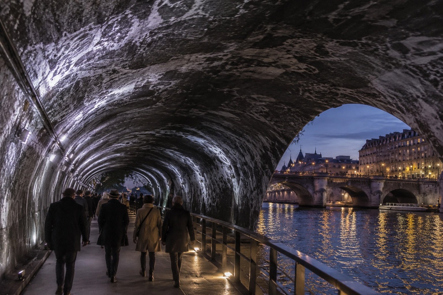 Dramatic cavern-like art installation wrapping an old stone bridge above a river at dusk